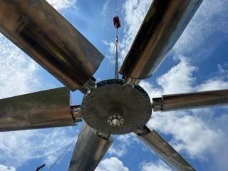 Fan being hoisted up for cooling tower installation. Blue skies in background.